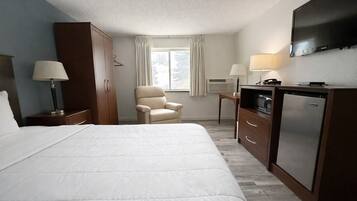 Ett hotellrum med en stor säng, en stol, ett skrivbord med en lampa, en TV och en minibar.