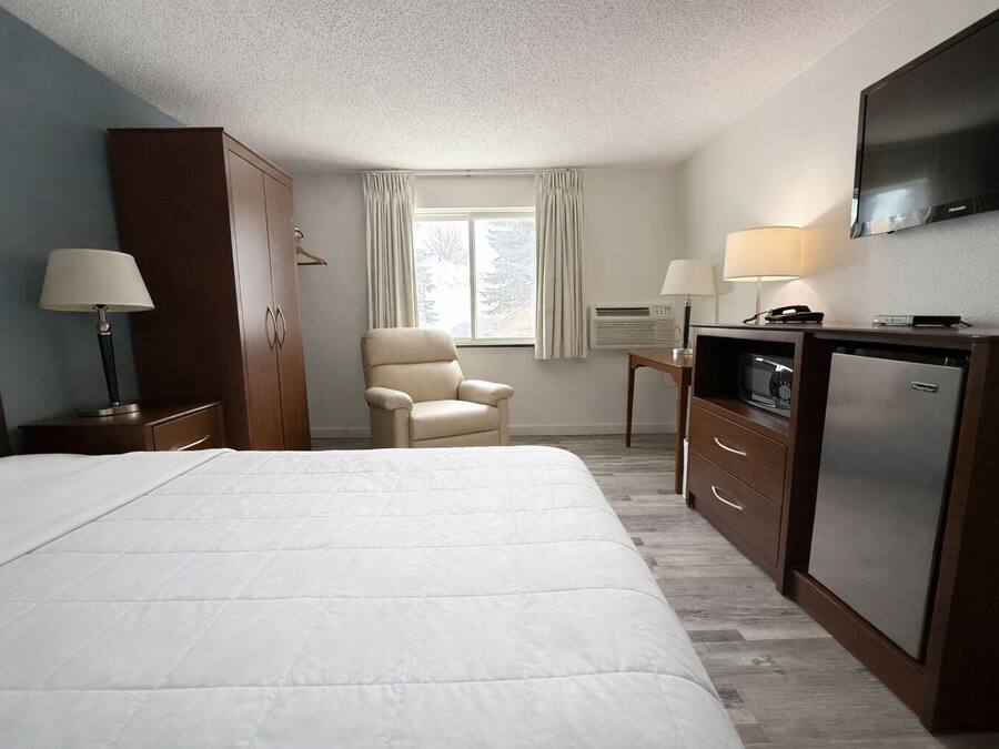 Ett hotellrum med en stor säng, en stol, ett skrivbord med en lampa, en TV och en minibar.