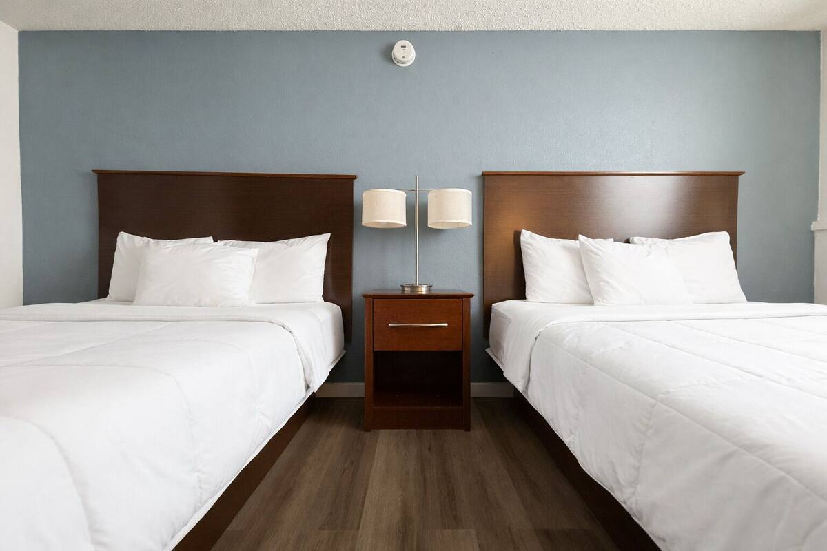 Une chambre d’hôtel avec deux lits, une table de chevet avec des lampes et un luminaire fixé au mur.