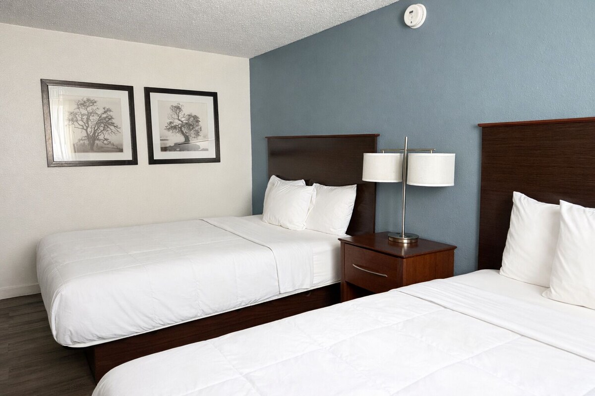 A hotel room with two beds, a nightstand with a lamp, and two framed pictures on the wall.