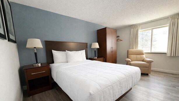 A hotel room with a large bed, two bedside tables with lamps, a wardrobe, a chair, and a window with curtains. - Hotel 8 (Fergus Falls)