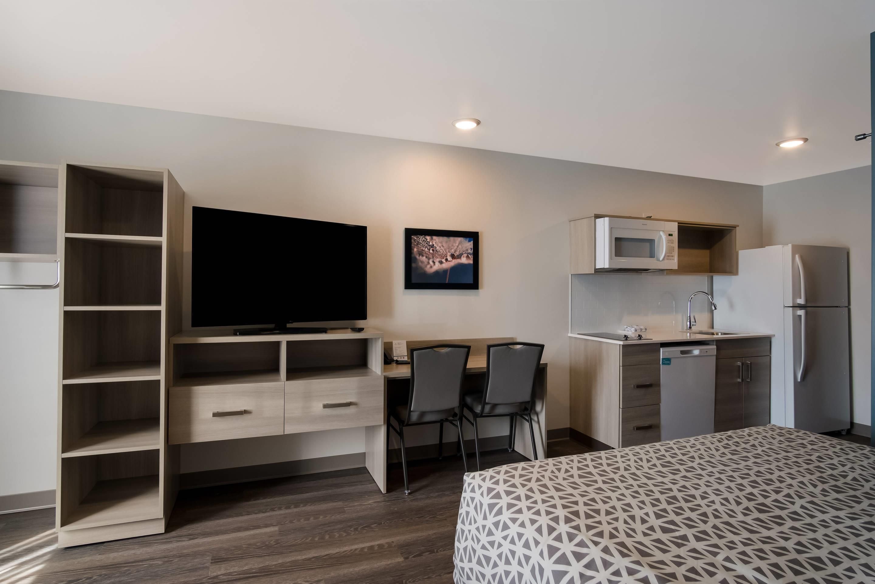 A compact hotel room with a bed, a desk with two chairs, a television, a microwave, a refrigerator, and a built-in wardrobe.