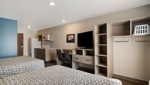 Una habitación de hotel con dos camas, kitchenette, televisor y armario.