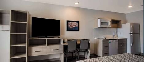 A compact hotel room with a bed, a desk with two chairs, a television, a microwave, and a refrigerator.