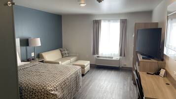 A hotel room with a bed, a sofa, a TV, a desk, and a window with curtains.