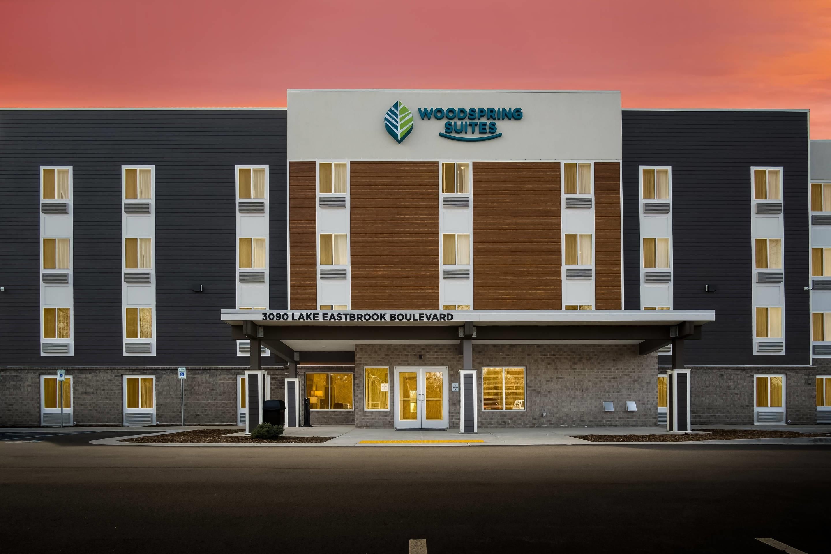A hotel with a modern facade, featuring a prominent logo and signage for 'Woodspring Suites' at the entrance.