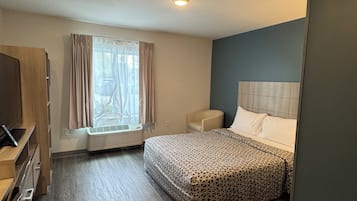 Una habitación de hotel con cama, una silla, un escritorio con computadora y una ventana con cortinas.