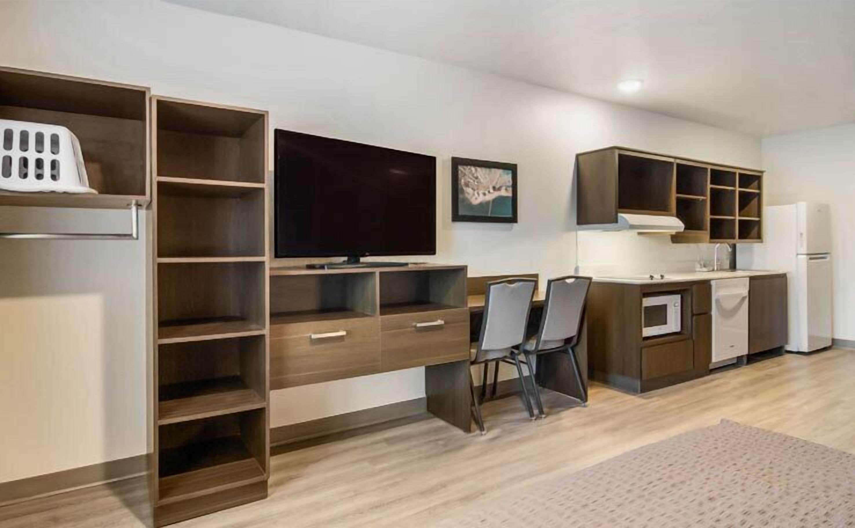 A modern kitchen with built-in appliances, a dining area with chairs, and a large TV on the wall.