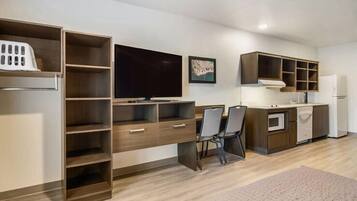 A modern kitchen with built-in appliances, a dining area with chairs, and a large TV on the wall.