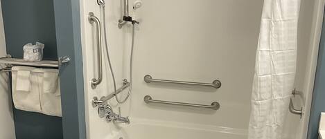 A walk-in shower with grab bars, a handheld showerhead, and a white shower curtain.