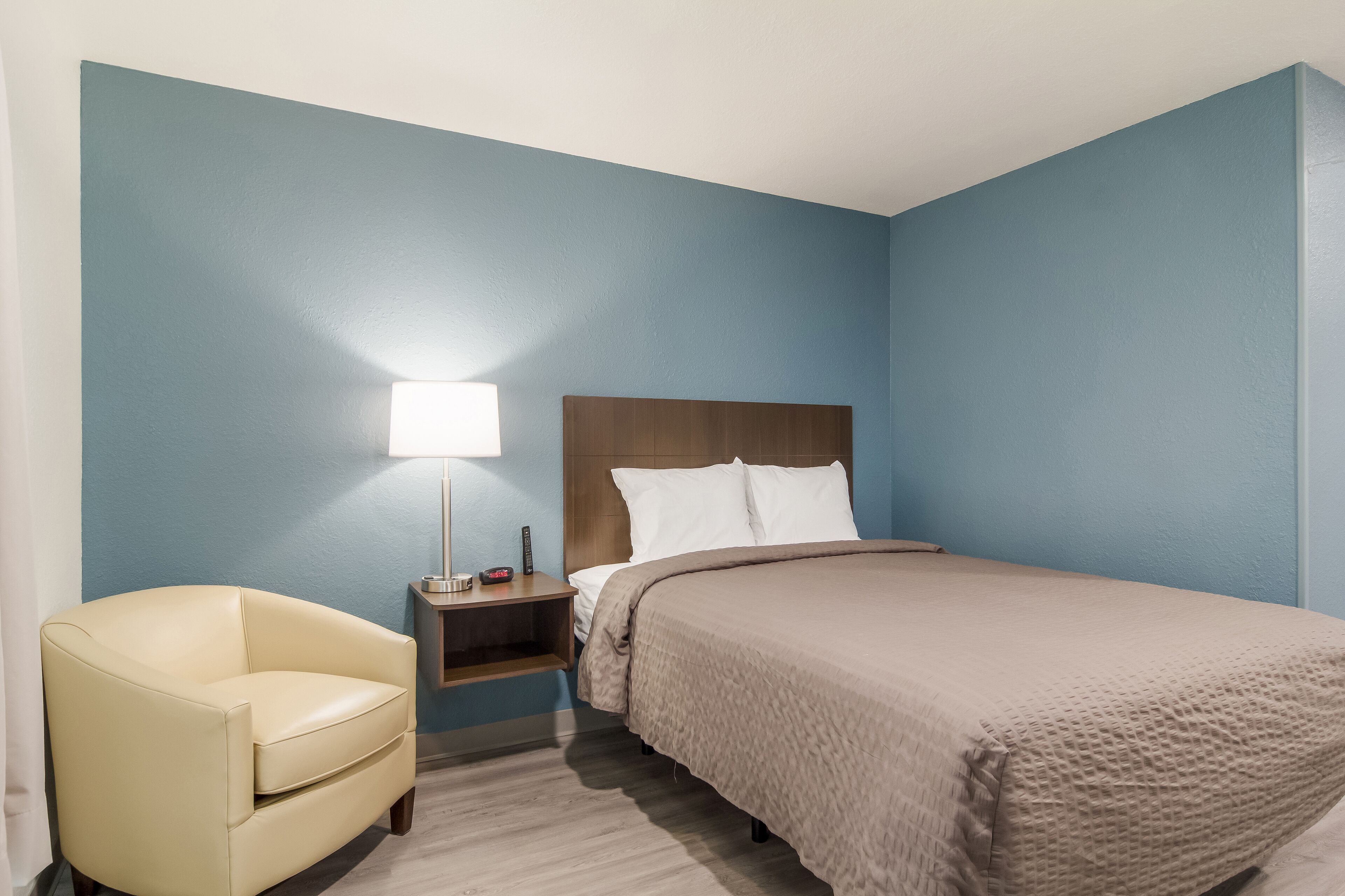 A hotel room with a bed, a nightstand, a lamp, and a chair.