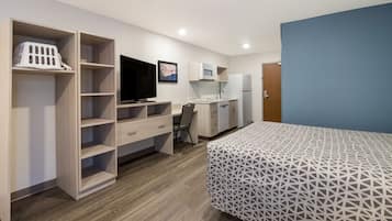 A compact room with a bed, a desk with a computer, a TV, and a kitchenette.
