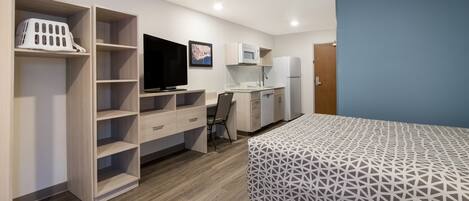 Une petite chambre comprenant un lit, un bureau avec un ordinateur, une télévision et une kitchenette.