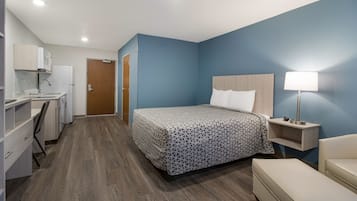 Une chambre d’hôtel comprenant un lit, une table de chevet, une lampe et un coin cuisine.