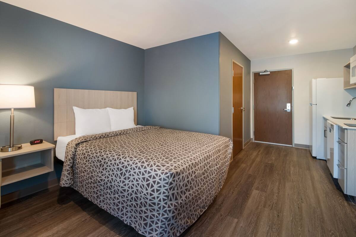 Une chambre d’hôtel équipée d’un lit, d’une table de chevet, d’une lampe et d’un coin cuisine.