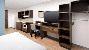 Quarto de hotel com cama, escrivaninha, televisão, armário e cozinha compacta.