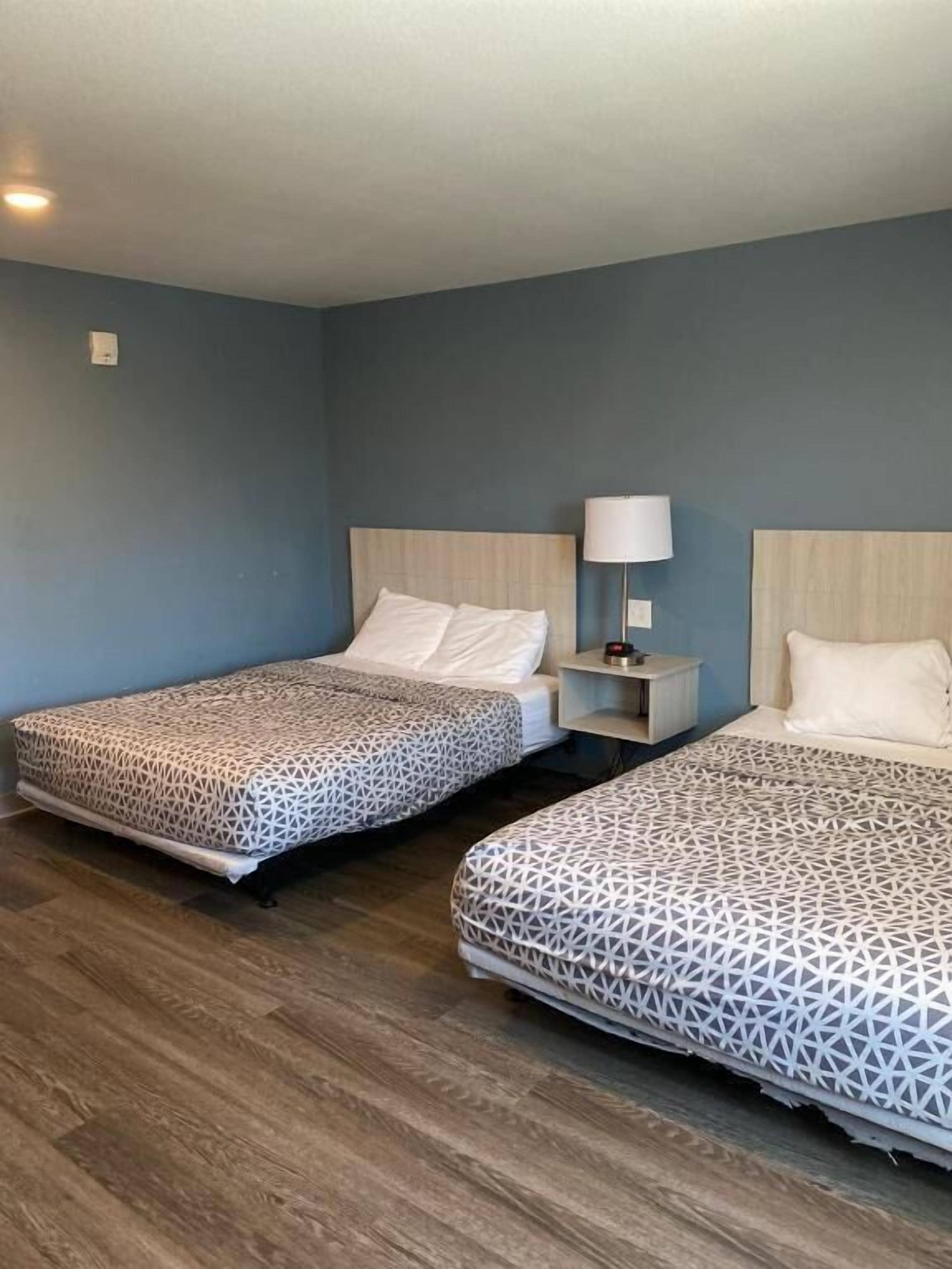 A hotel room with two beds, a nightstand with a lamp, and a wooden floor.