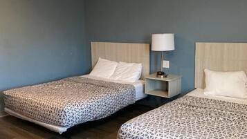 A hotel room with two beds, a nightstand with a lamp, and a wooden floor.