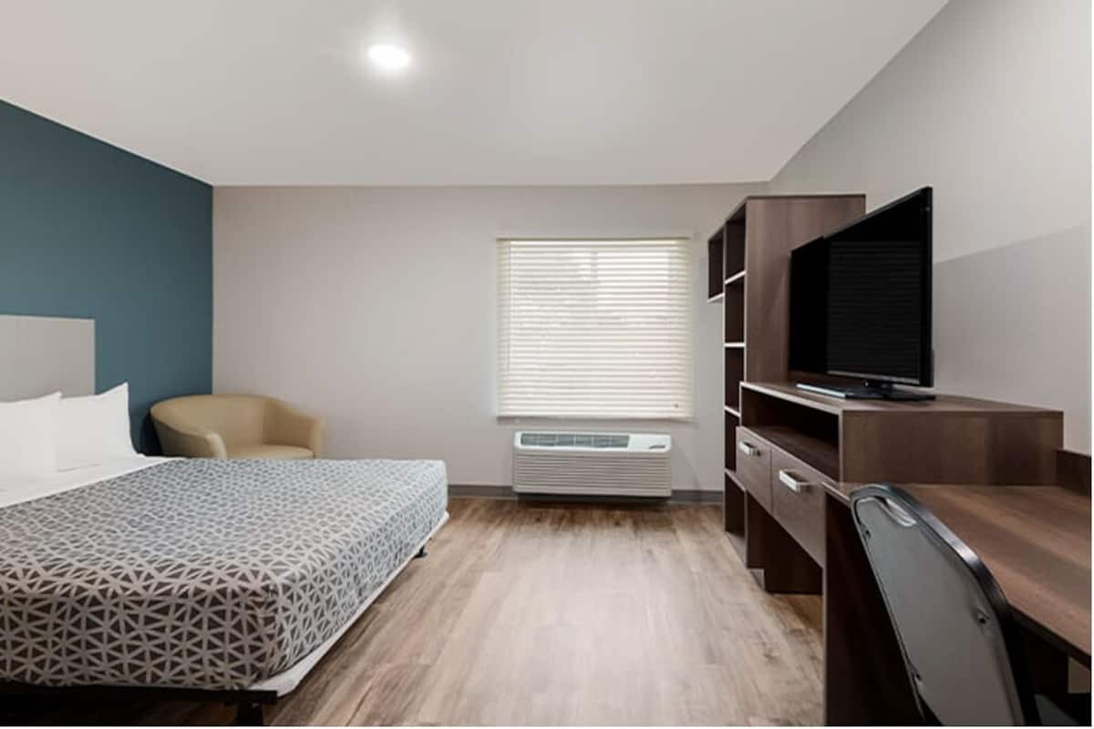 Une chambre d’hôtel moderne équipée d’un lit, d’un bureau, d’une chaise, d’une télévision et d’une fenêtre avec des stores.