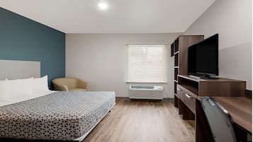 A modern hotel room with a bed, a desk, a chair, a television, and a window with blinds.