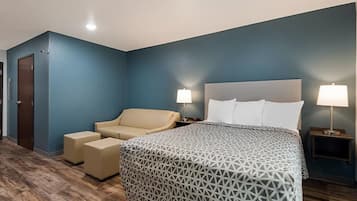 A hotel room with a bed, a sofa, two bedside tables with lamps, and a door.