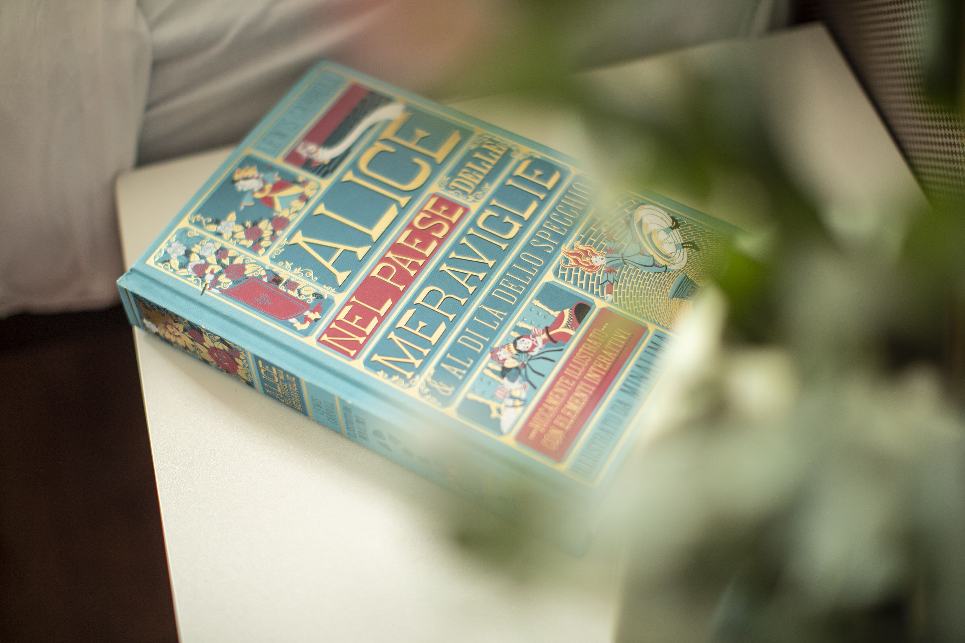 Un libro con el título 'Alice's Adventures in Wonderland' sobre una superficie blanca.