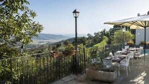Een terras buiten, met tafels en stoelen, omgeven door groen en een mooi uitzicht.