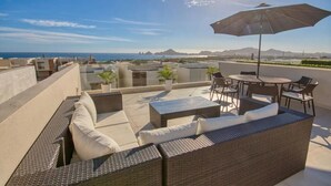 Una terraza en la azotea con muebles de mimbre, una mesa y una sombrilla.