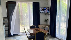 En matplats med ett runt bord, stolar och en soffa. På väggen sitter en tv, och en trappa leder ut till ett område utomhus.