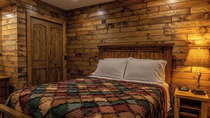 A bedroom with a wooden wall panel design, a bed with a colorful quilt, white pillows, and a bedside table with a clock. - Phelps Lakeview Lodge Holiday House (Phelps)