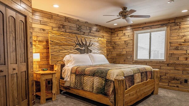 A bedroom with a wooden headboard, a bed with a quilt, a nightstand, a wall clock, and a window with blinds. - Phelps Lakeview Lodge Holiday House (Phelps)