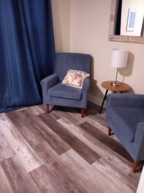 A room with a blue armchair, a smaller armchair, a wooden floor, a lamp, and a mirror on the wall. - Modern Home, Great Deck & Yard- Peaceful at Potter (Mobile)