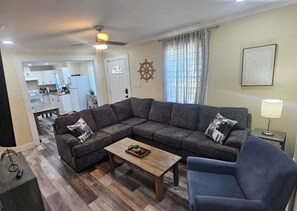 A living room with a sectional sofa, a coffee table, and a TV stand. - Modern Home, Great Deck & Yard- Peaceful at Potter (Mobile)