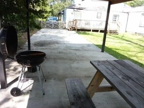 Un jardin avec un barbecue, une table de pique-nique et une maison en arrière-plan.