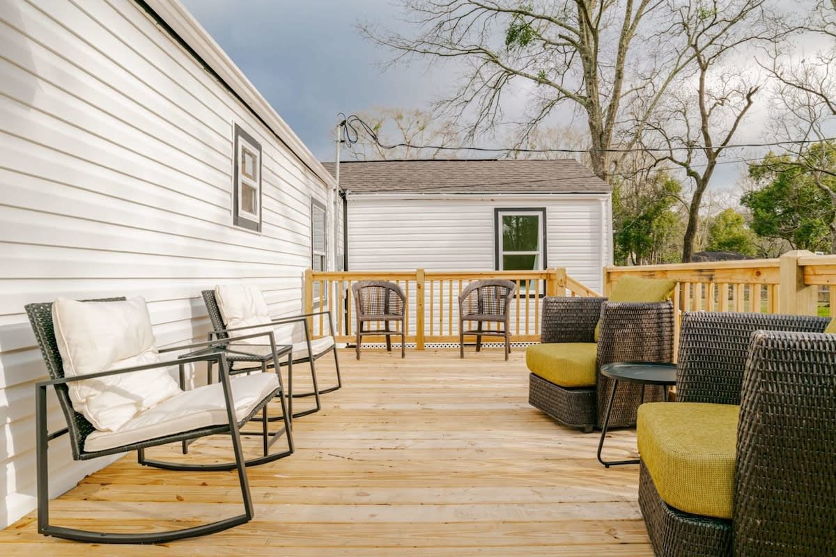 Une terrasse en bois, agrémentée de mobilier d’extérieur, notamment des chaises et une table, jouxtant un bâtiment blanc.