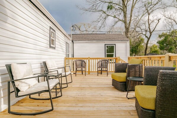 A wooden deck with outdoor furniture, including chairs and a table, adjacent to a white building. - Modern Home, Great Deck & Yard- Peaceful at Potter (Mobile)
