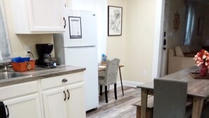 Una cocina con armarios blancos, una mesa de comedor con sillas y un refrigerador.