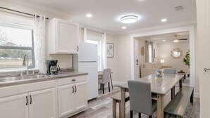 Une cuisine moderne avec des meubles blancs, un appareil à café intégré et un coin repas comprenant une table et des chaises en bois.