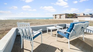 A beachside patio with white furniture and a view of the ocean.