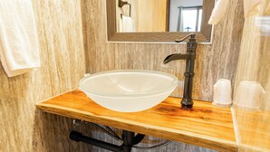 Een badkamer met een houten wastafelmeubel, een glazen wasbak, een zwarte kraan en een spiegel met een reliëf lijst.