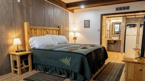 Een kamer met houten lambrisering, een bed, bedlampjes, een houten nachtkastje, een klein tafeltje en een spiegel.