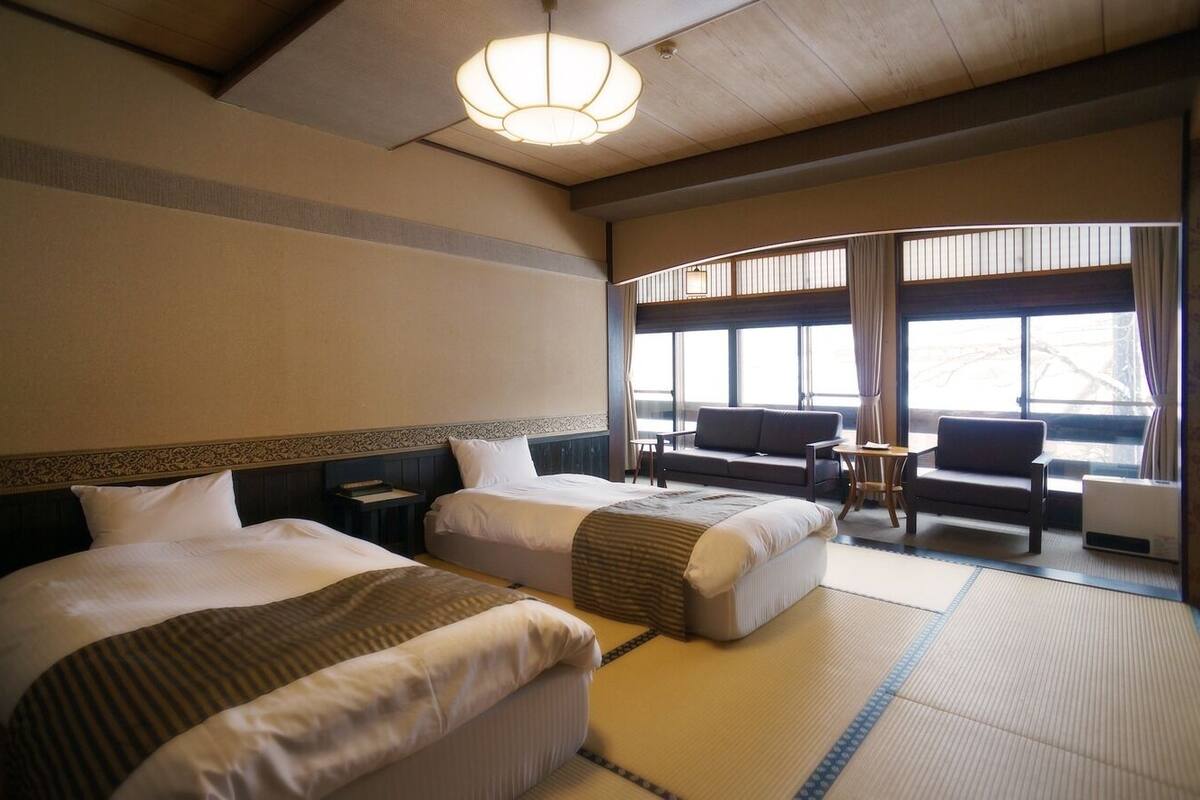 A hotel room with two beds, a sofa, a small table, and large windows.