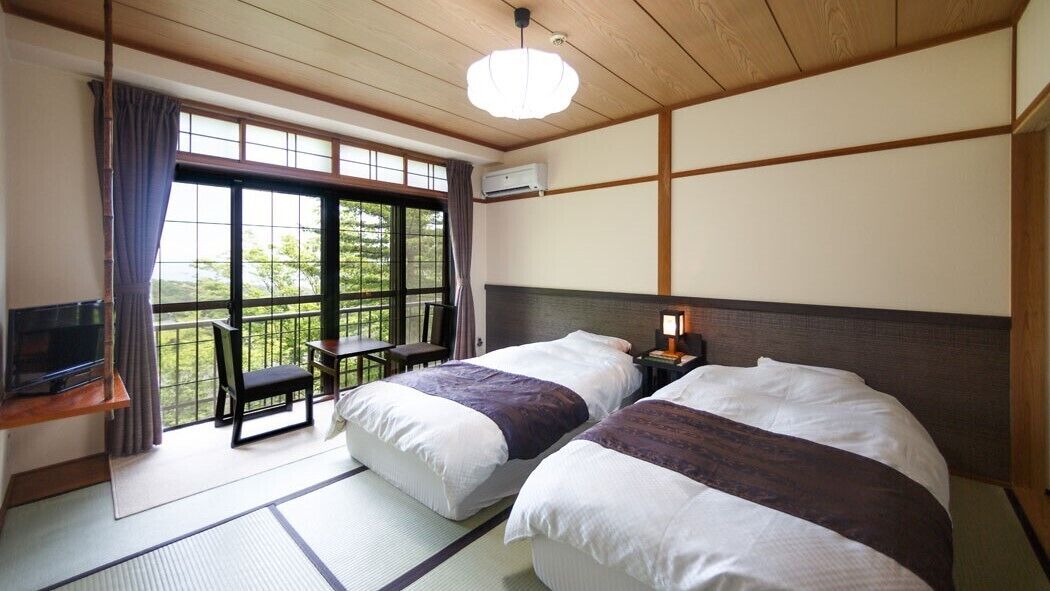 A traditional Japanese room with tatami flooring, two beds, a desk, and a television.