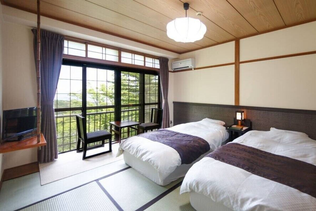 A traditional Japanese room with tatami flooring, two beds, a desk, and a television.