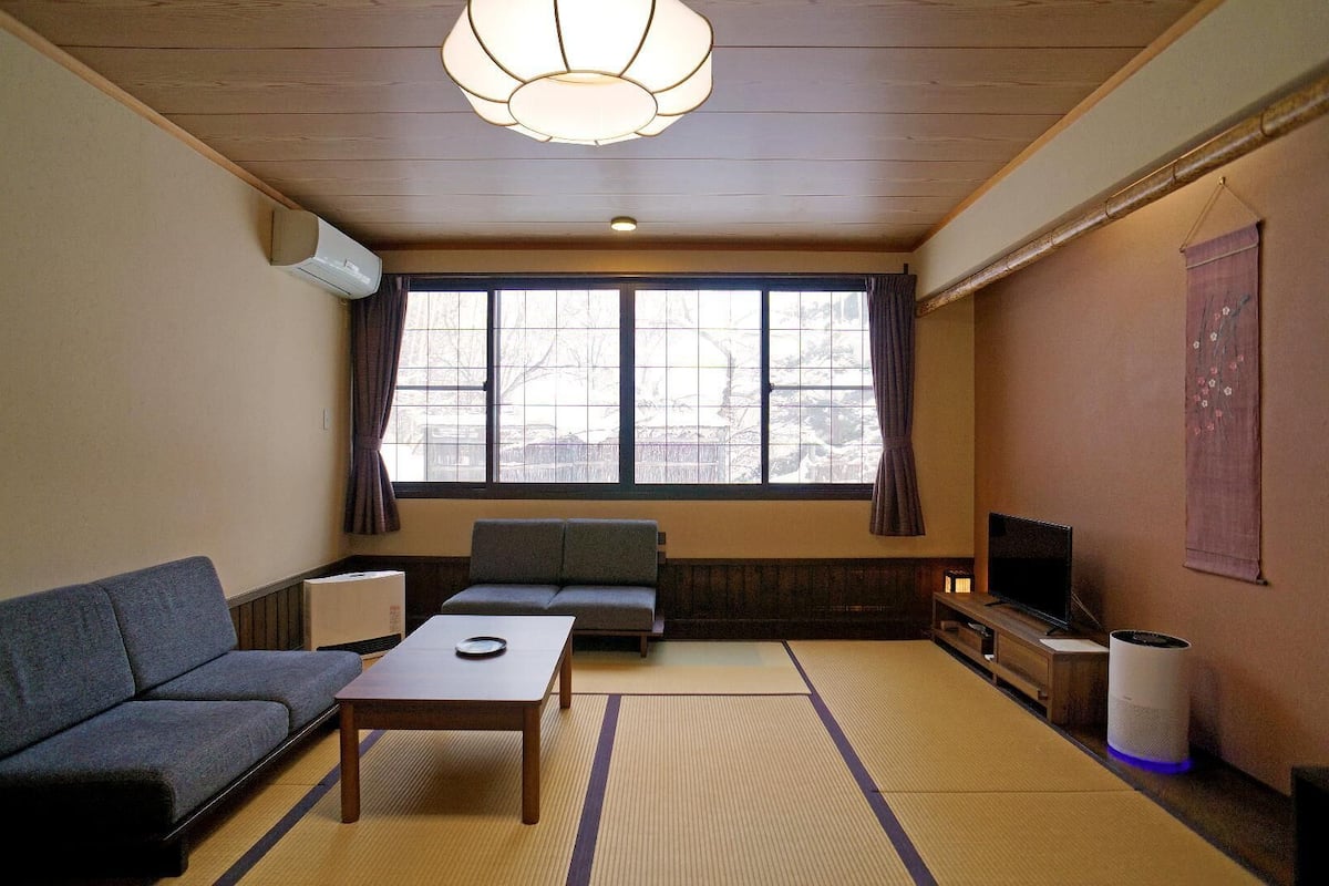 A room with a sofa, a table, a television, and tatami mats.