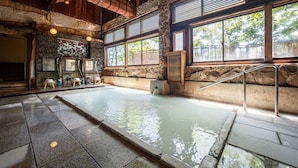 Ein traditionelles japanisches Onsen mit Steinwänden, Holzbalken und einem Steingrundschwefelbad.