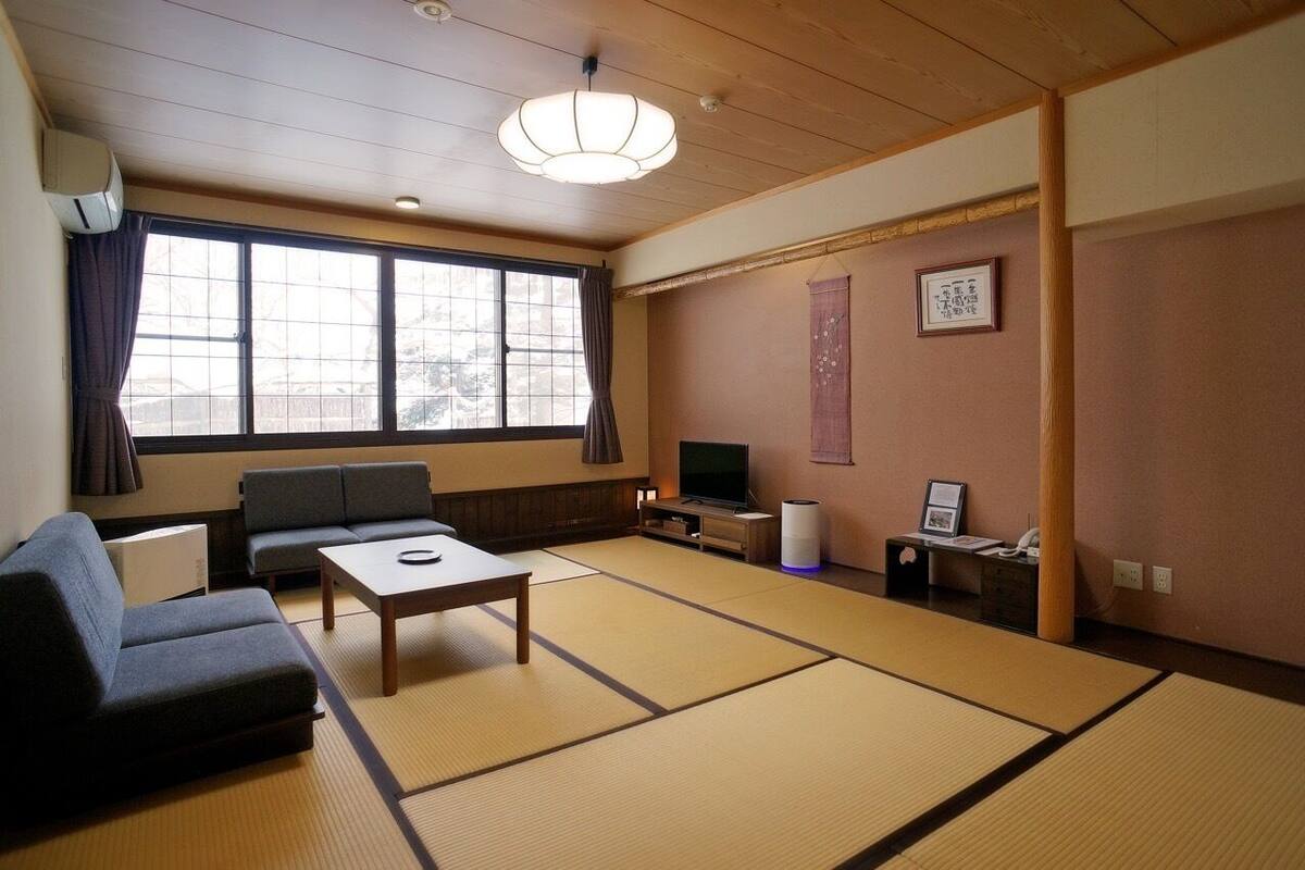 A traditional Japanese-style room with tatami flooring, a sofa, a television, and a sliding door.