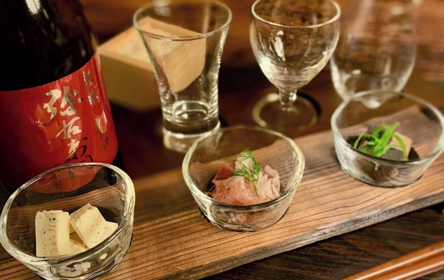 A wooden table with clear glass bowls containing food items, a bottle, and glasses.