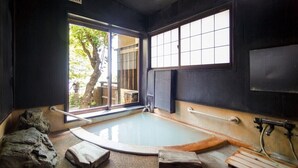 Ein traditionelles japanisches Onsen mit einem Steingrotte-Bad, Holzliegen und Blick auf einen Baum.