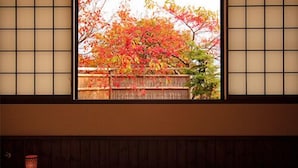 Ein traditioneller japanischer Raum mit Tatami-Böden, einem niedrigen Tisch mit Teeservice und Blick auf Herbstlaub durch einen Shoji-Bildschirm.